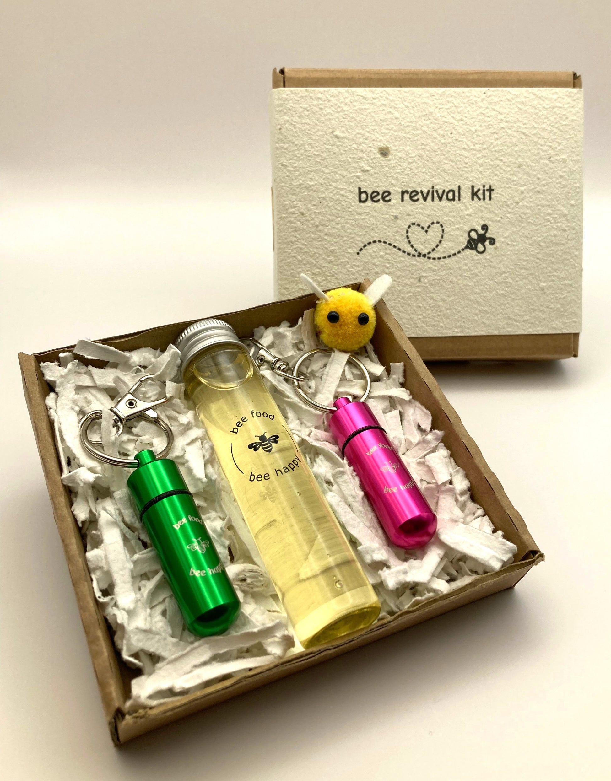 Showing bee revival kit box, opened showing the contents, consisting of glass bottle with 20ml Inveråtbee syrup, two bee revival keyrings, seed paper packing and a cute little fabric bee.