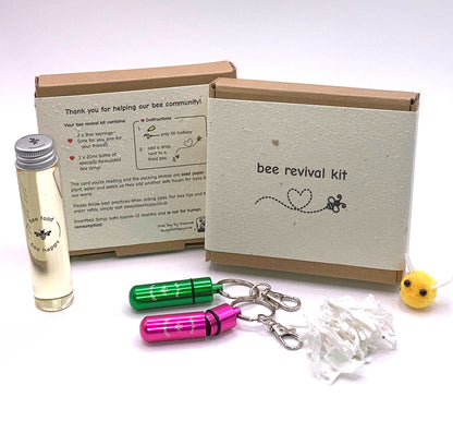 Showing the front and back of the bee revival kit box, together with the contents sitting next to it. Contents consisting of glass bottle with 20ml Invertbee syrup, two bee revival keyrings, seed paper packing and a cute little fabric bee.